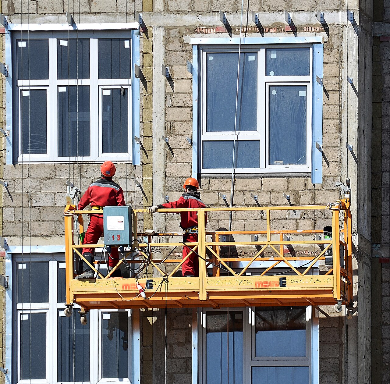 Workers on a suspended scaffold fixing rainscreen brackets to an apartment building