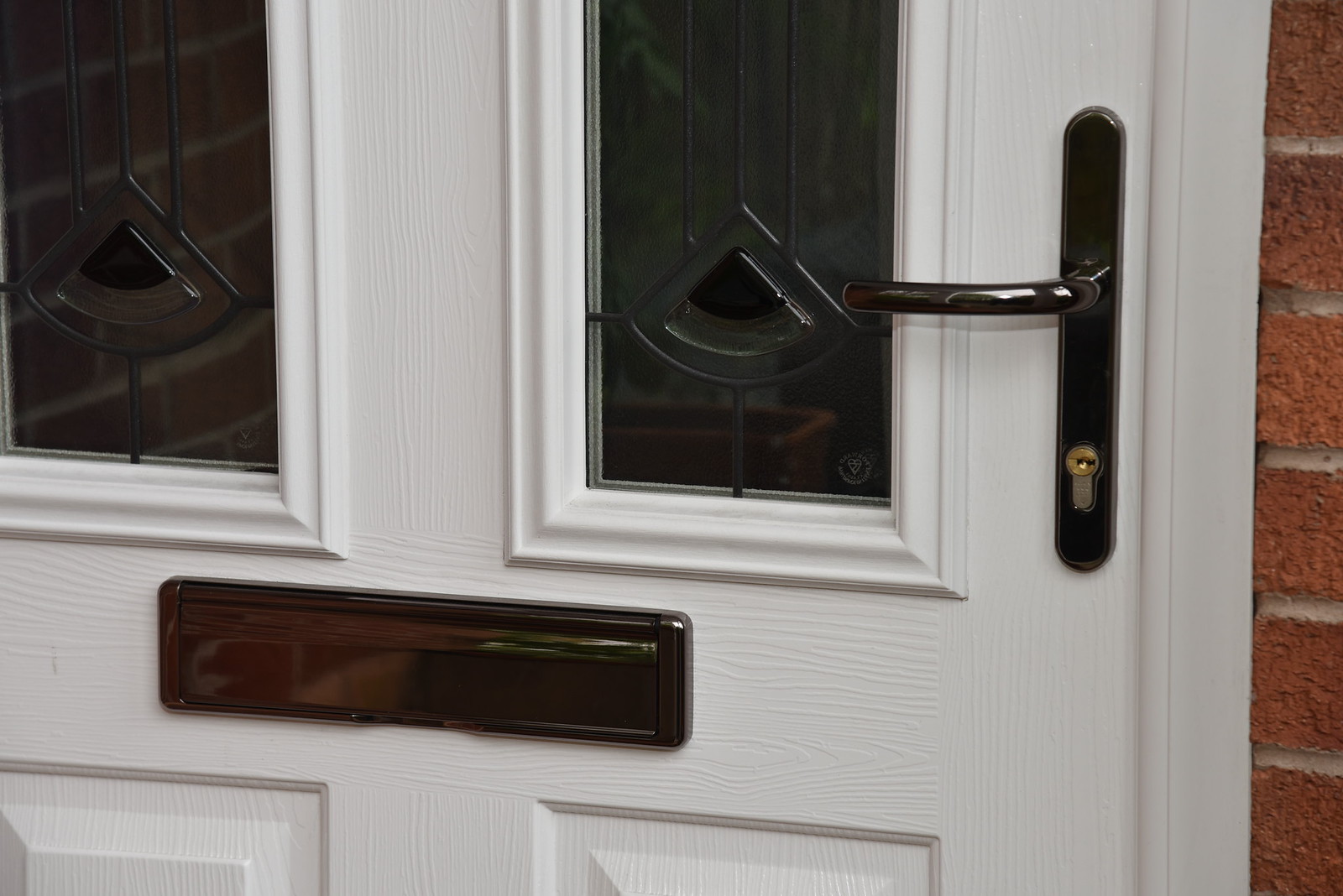 A white composite front door with two decorative glazed panels, a dark handle, lock and letterbox