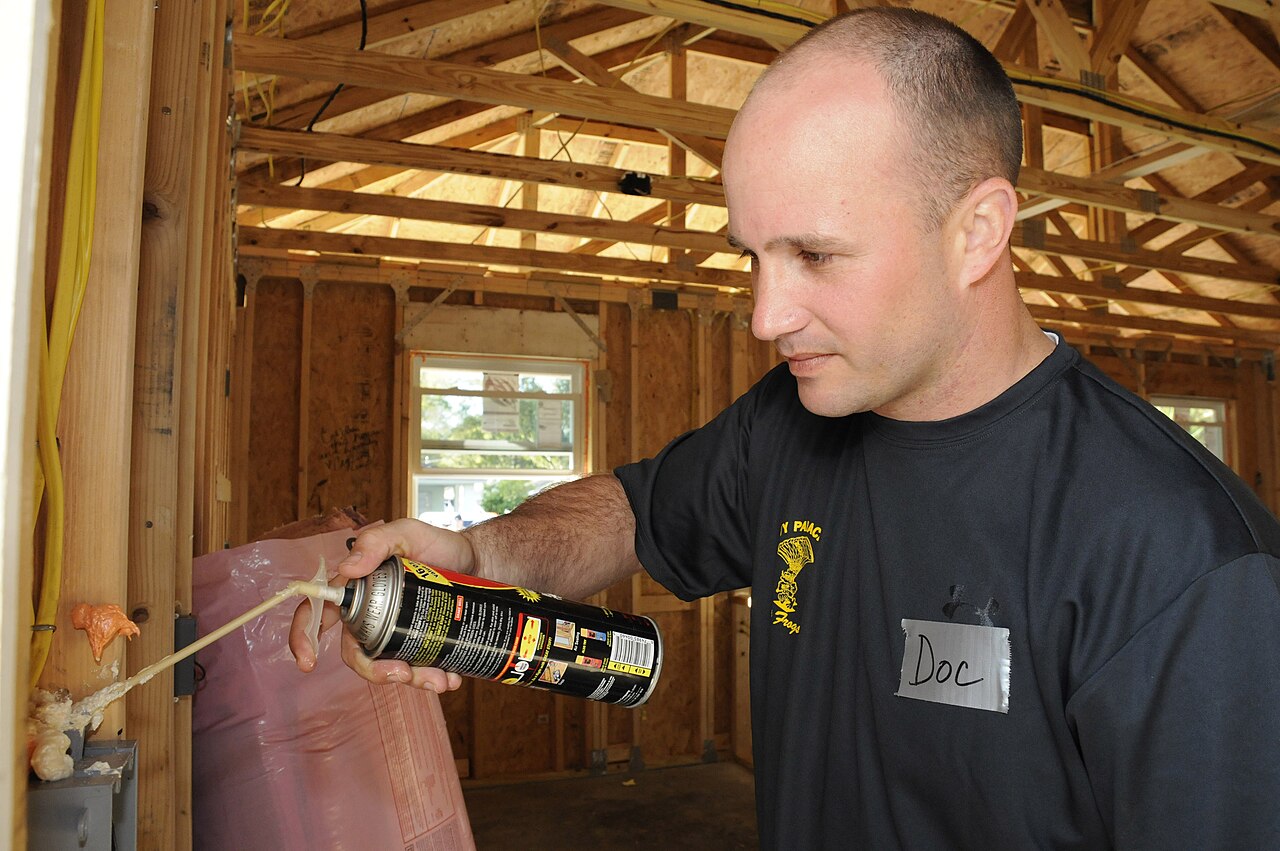 A volunteer spraying foam insulation into timber framing on a house construction site