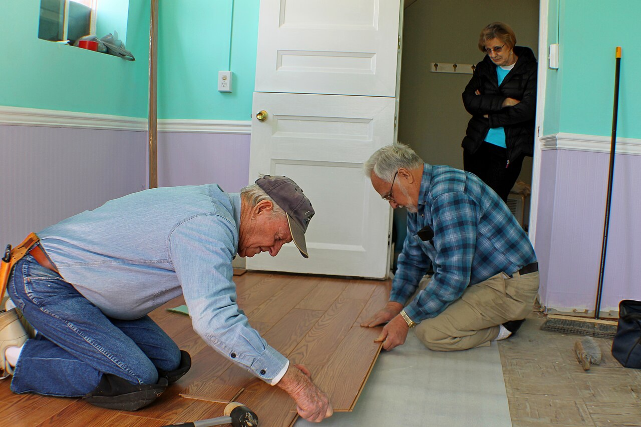 Close-up of laminate planks being assembled over underlay, showing the tongue and groove joint and the gap kept from the wall