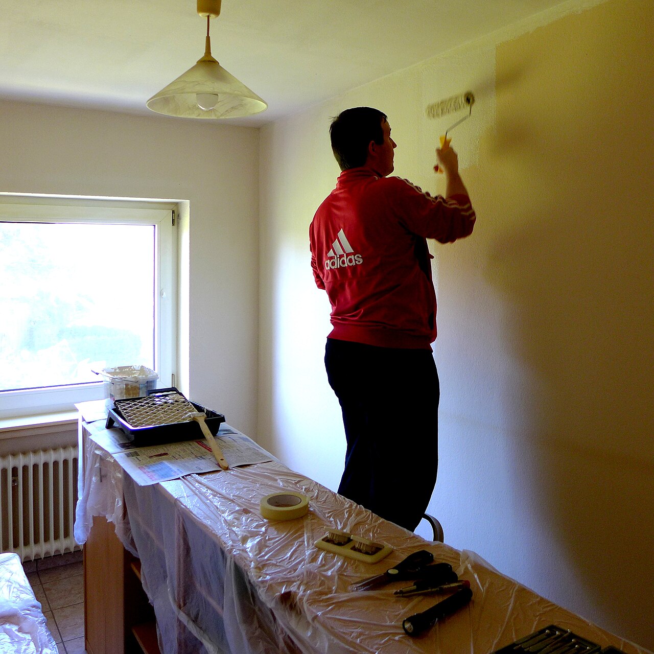 A person painting an interior wall with a paint roller