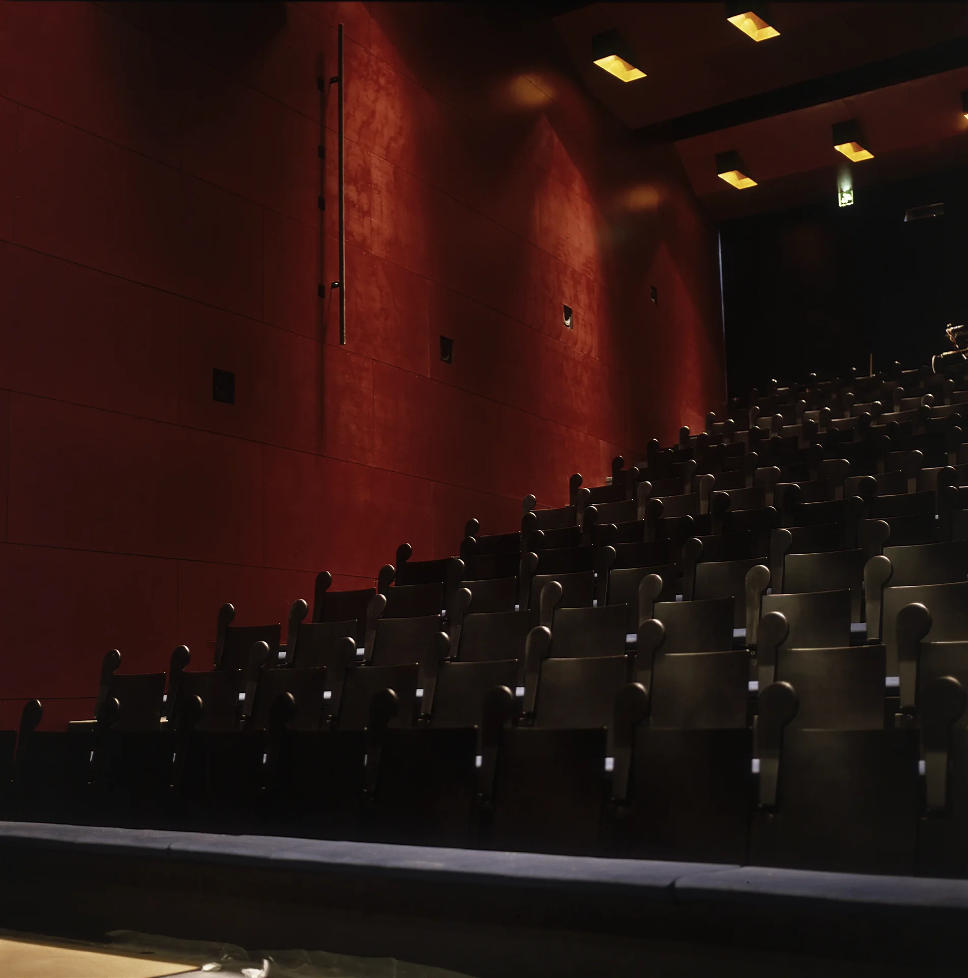 Theatre auditorium with walls clad in red plywood panels and rows of blue upholstered seats
