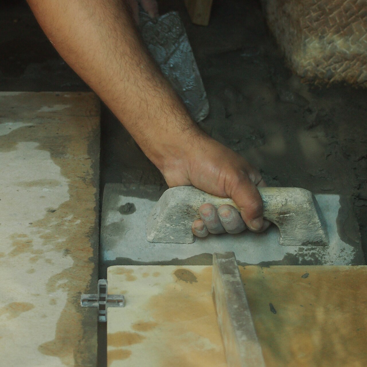 A tiler spreading adhesive with a notched trowel before laying floor tiles