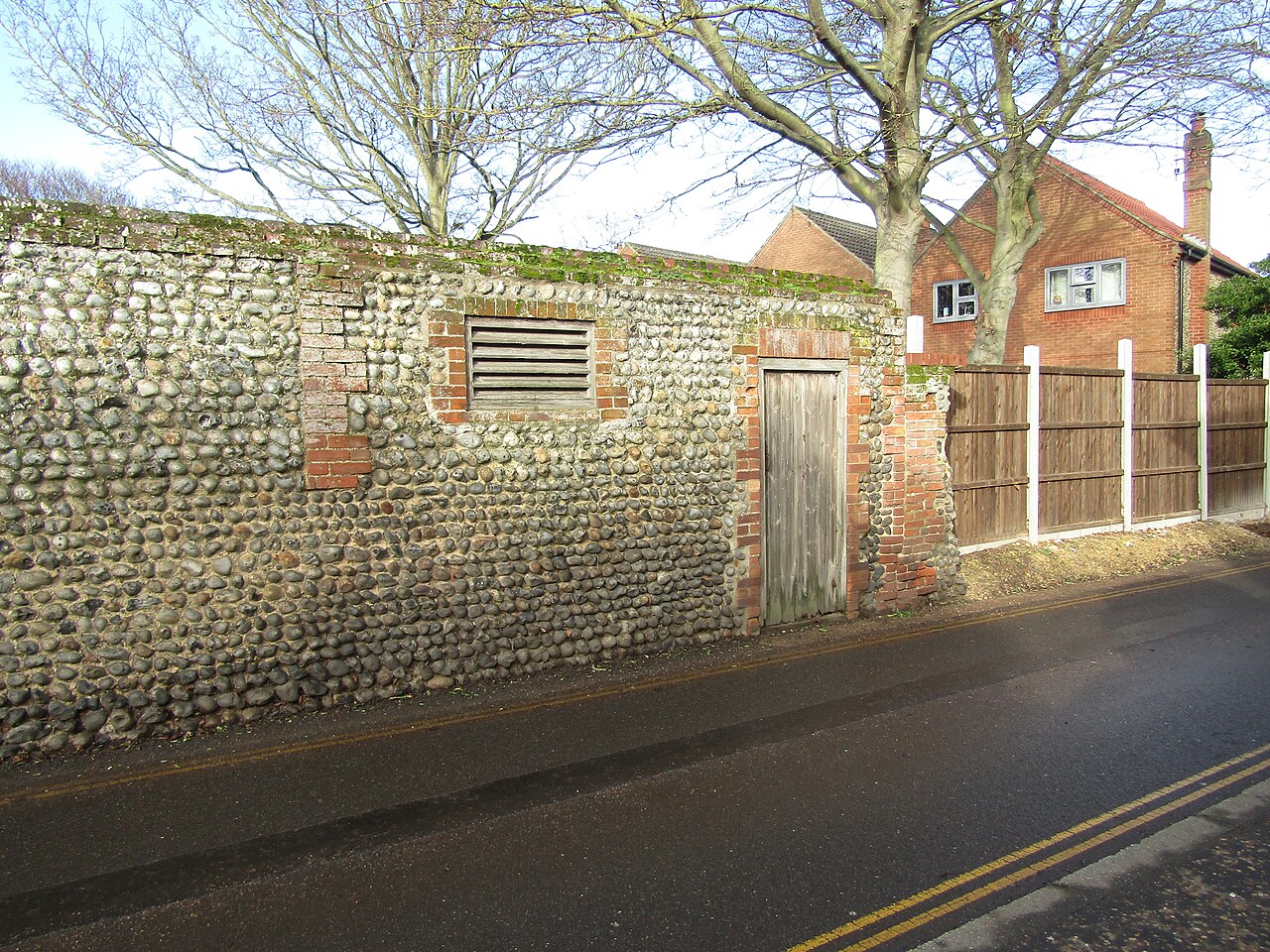 A brick and flint wall with a doorway and a louvred opening, High Street, Mundesley, Norfolk