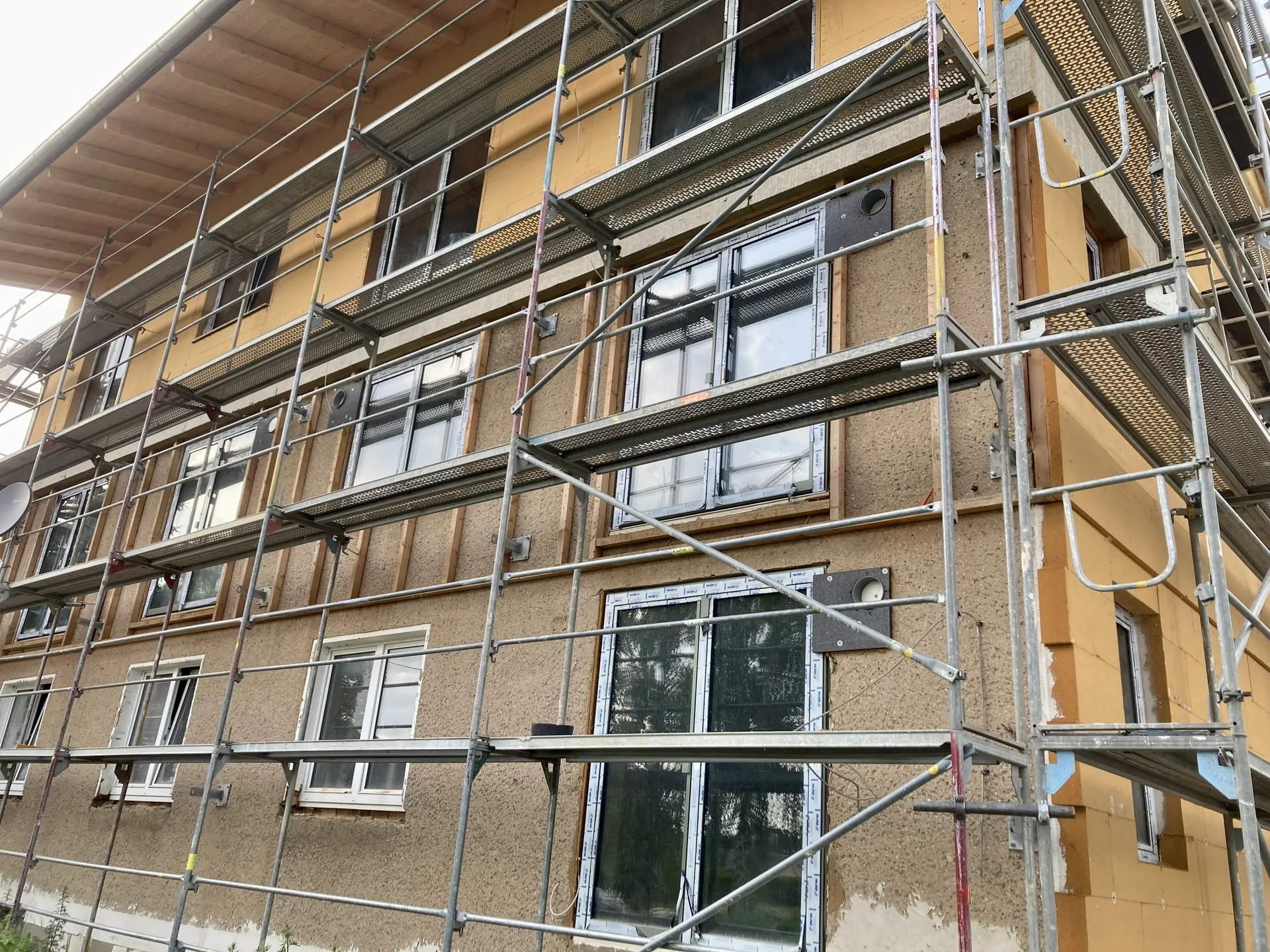 Wood fibre insulation boards fixed to the facade of a house, with base plates for fixing balconies