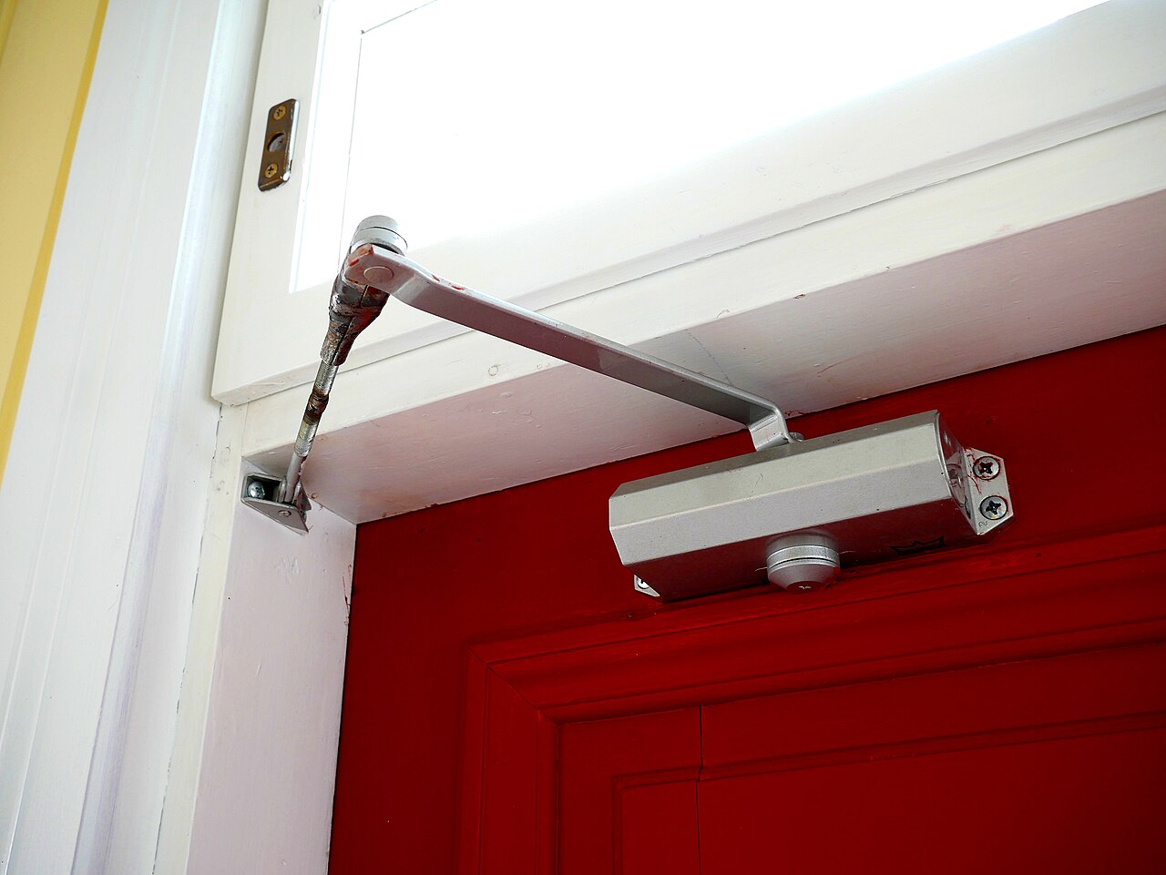 A surface-mounted overhead door closer and arm on a door