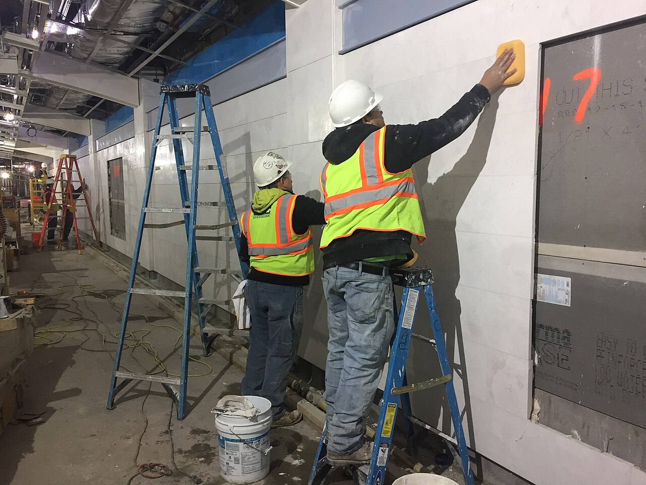 Tile finishes being grouted along a passenger corridor in a station concourse under construction