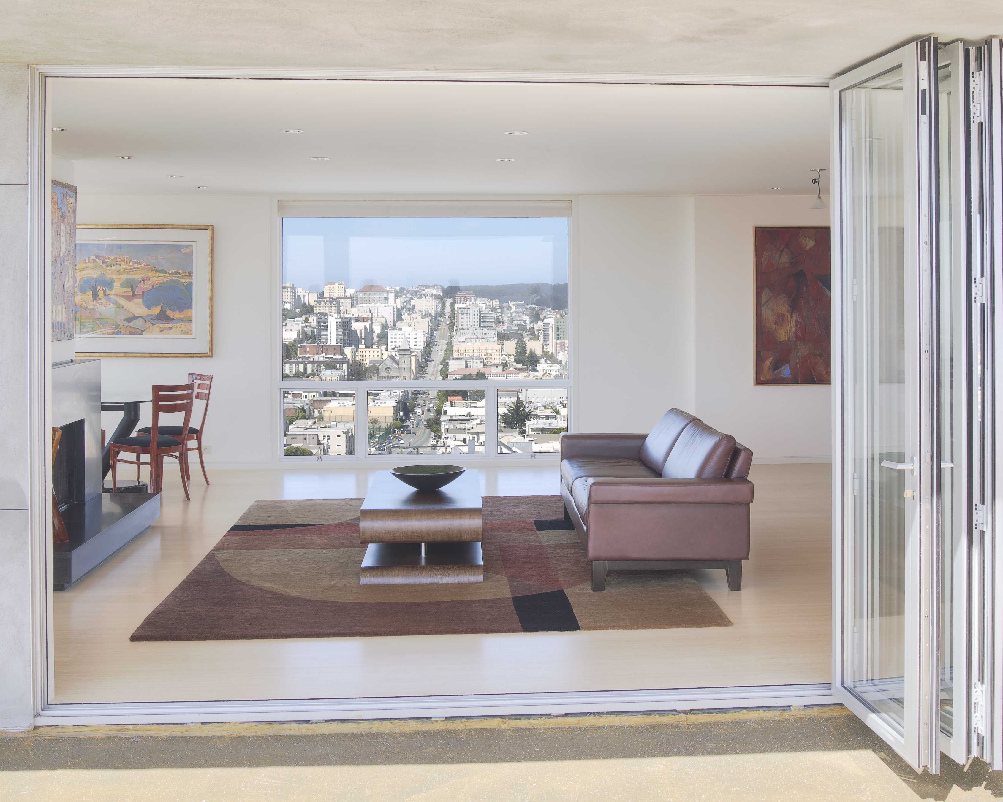 A white-framed glass folding wall stacked open at one side of a bright living room, opening onto a balcony