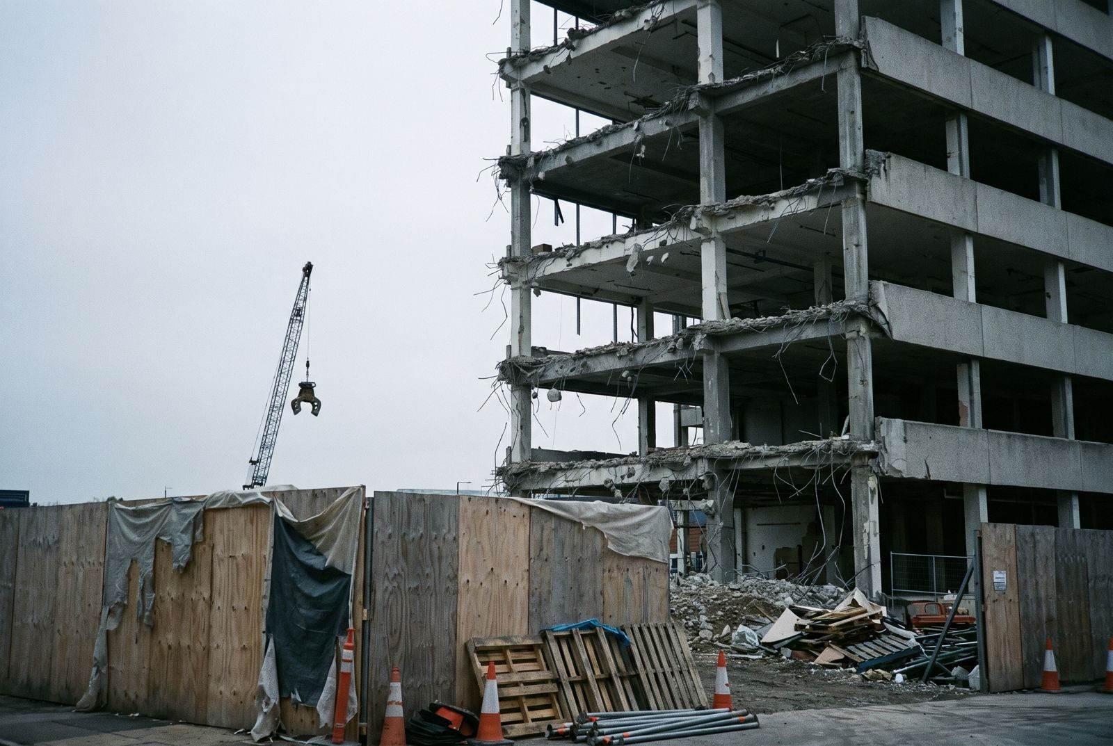 Partially demolished concrete frame building behind site hoarding